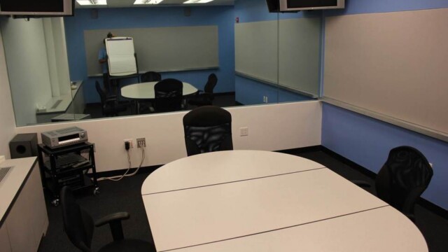 Focus group room with small conference table and chairs, blue walls, and mirror.