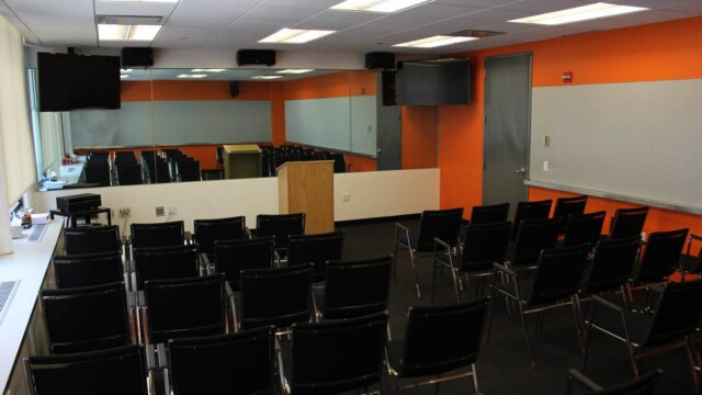 Focus group room that is configured theater style with black arm chairs lined in rows facing the mirror.