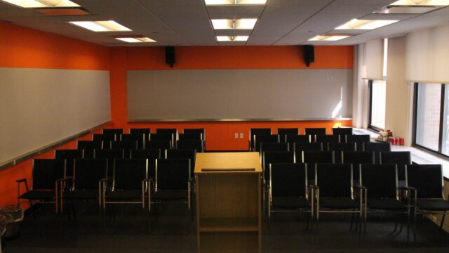 Focus group room configured theater style with rows of black arm chairs facing a podium.