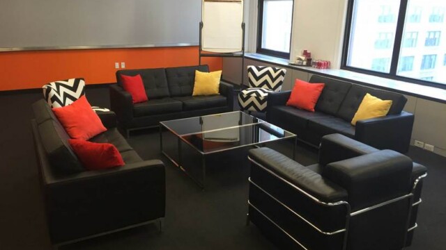 Focus group room configured in a living room setup consisting of modern black sofas and showing the wall of windows.
