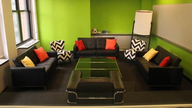 Focus group room configured in a living room setup consisting of modern black sofas and showing the 1 tackable wall and windows.