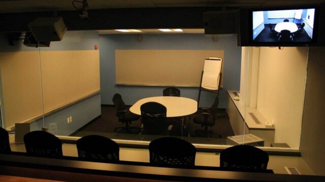 View of a focus group room from the viewers perspective including no overhead lights and only dim countertop lighting that provides task lighting for people sitting at desks observing the research.