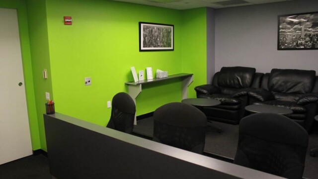 Viewing room at focus group facility showing 2 tiers of desktop with multiple office chairs, green walls, and soft seating.