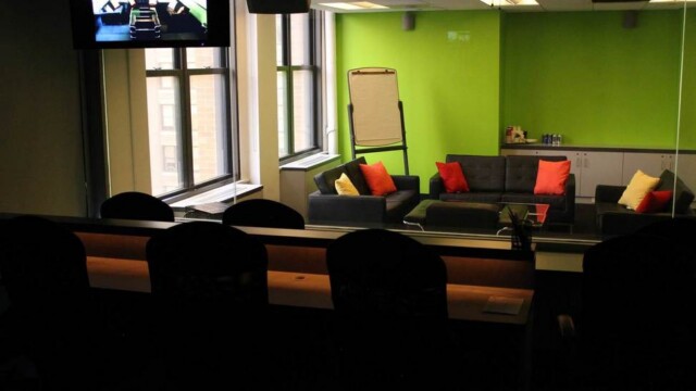 View of a focus group room from the viewers perspective including no overhead lights and only dim countertop lighting that provides task lighting for people sitting at desks observing the research. Focus group room configured with living room furniture.