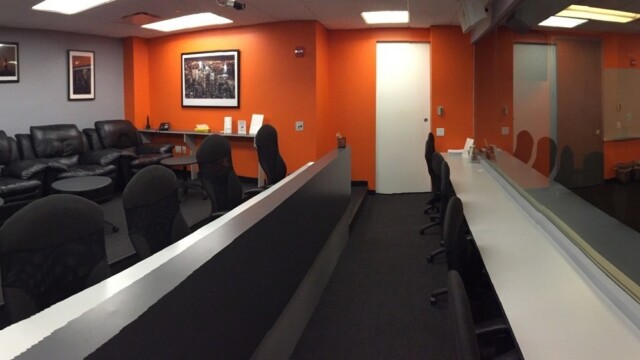 Panoramic view of a focus group facility viewing room showing 2 tiers of desk chairs and countertops and a third tier that has oversized black leather arm chairs.